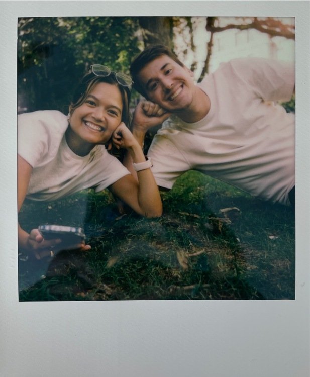 polaroid photo of two people lying on the ground using a phone as a remote