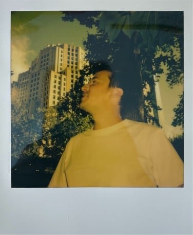 polaroid photo of a man with a city building behind him